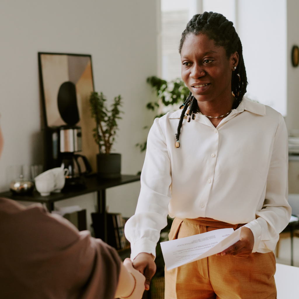 Image of a lady formally dressed, holding a document on the left hand, shaking hands with another person (image not shown). Stock image used to build relevance to the blog "visitor to work permit in Canada", within the Francophone work permit section.